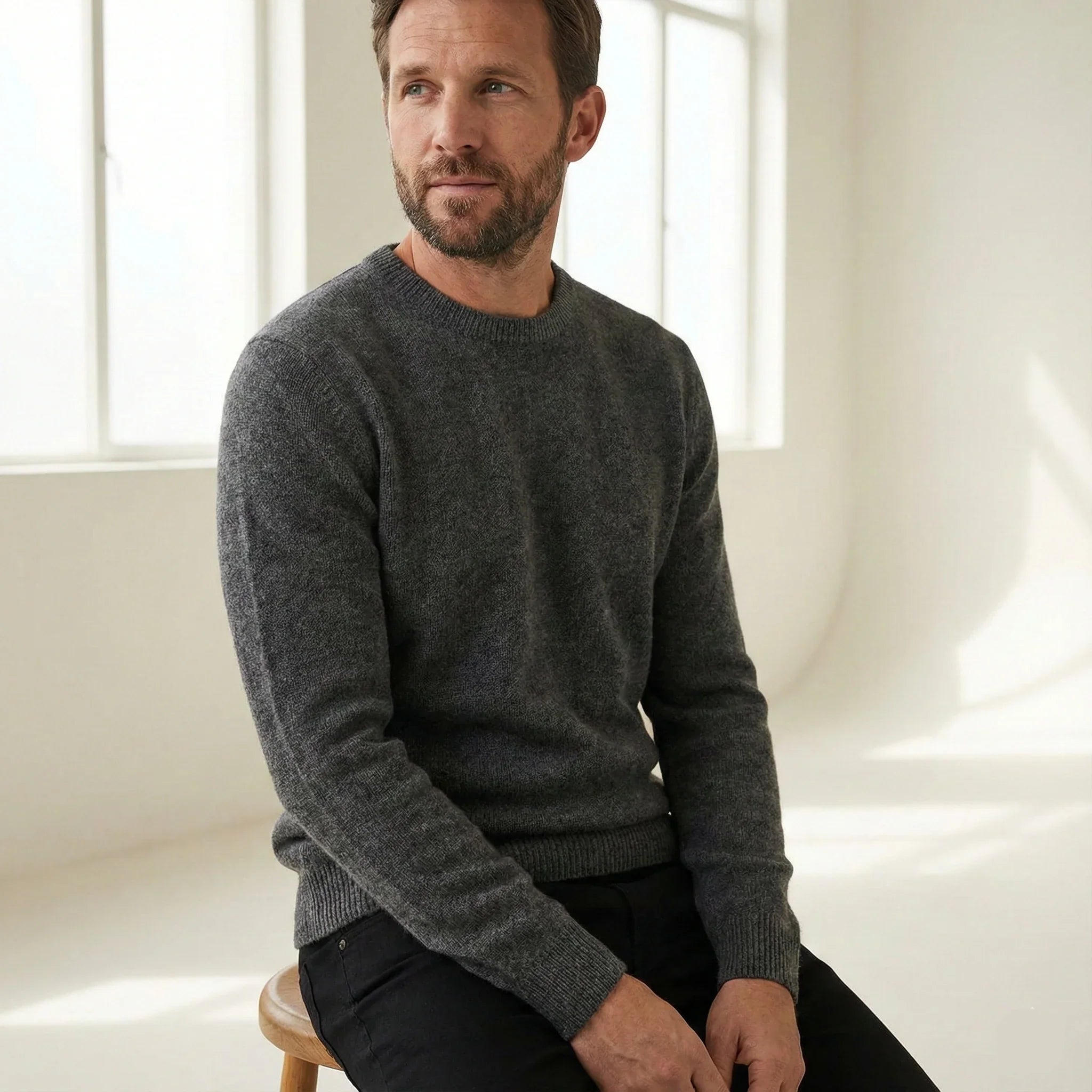Man wearing a gray crewneck sweater and black pants in a bright minimalist room