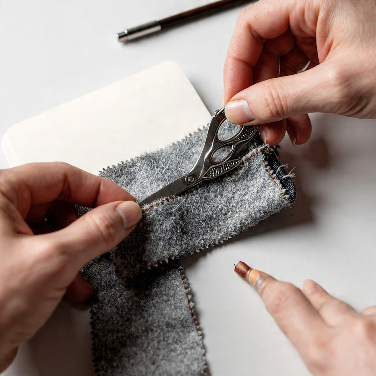 Person cutting fabric with scissors on a white surface

