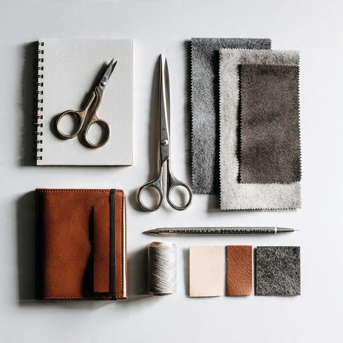 Harlan Forge brand story – flat-lay of design tools and fabric on white background.